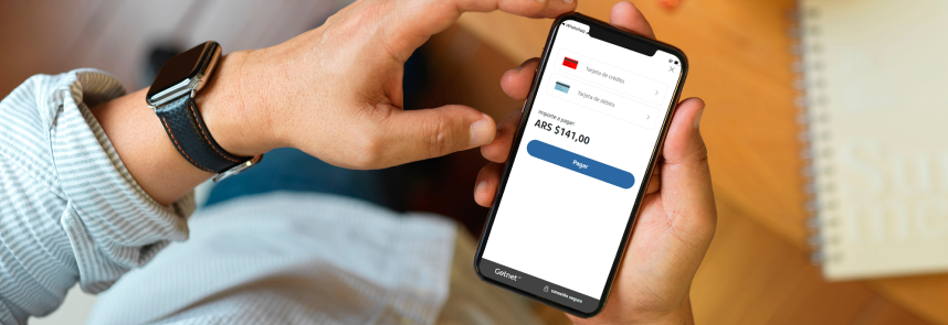 Persona sosteniendo un teléfono móvil que muestra la pantalla de pago con opciones de tarjeta de crédito y débito, el importe $141,00 y el botón azul ‘Pagar’.