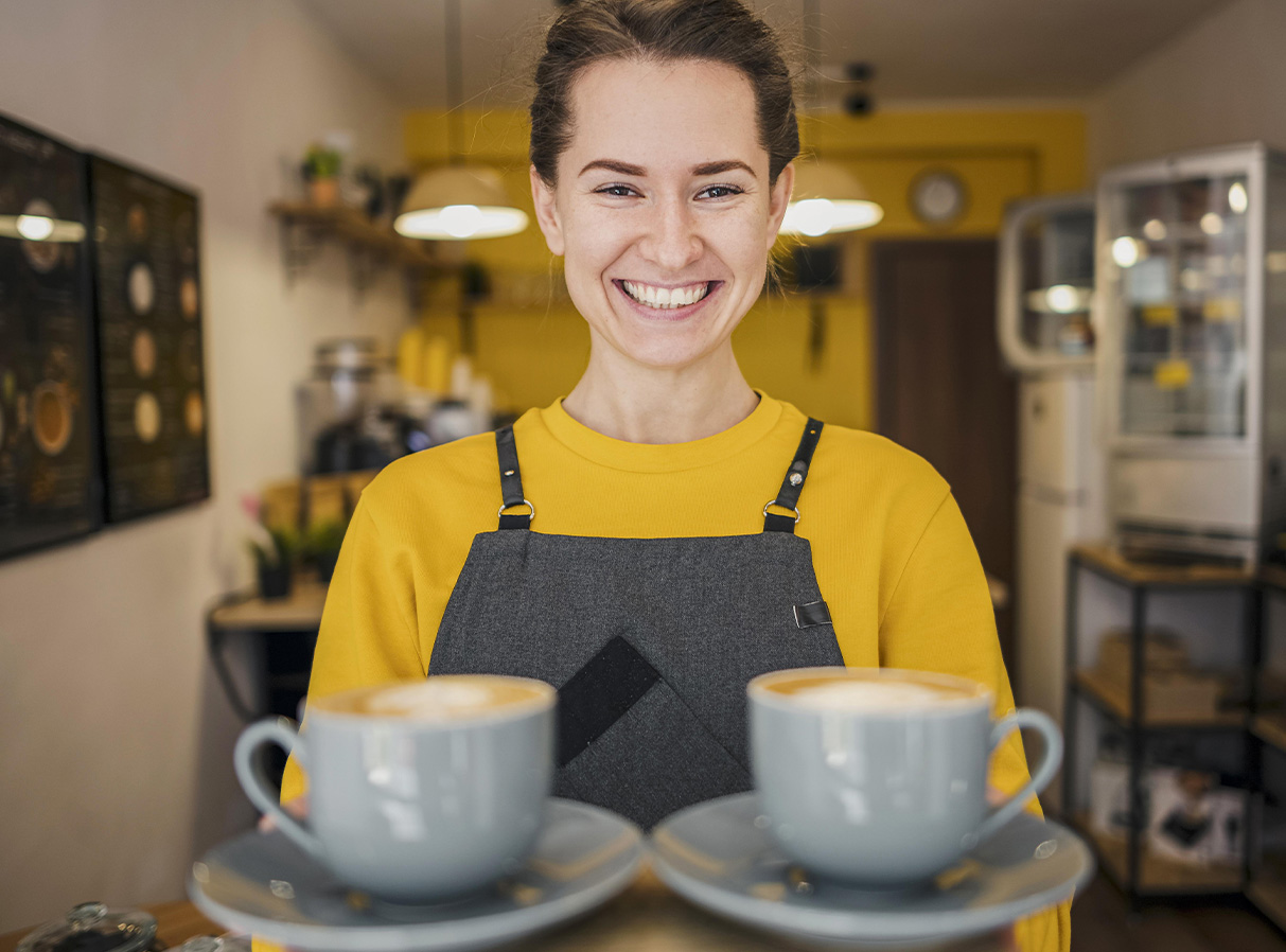 Persona sosteniendo dos cafés con guardapolvo en una cafetería.