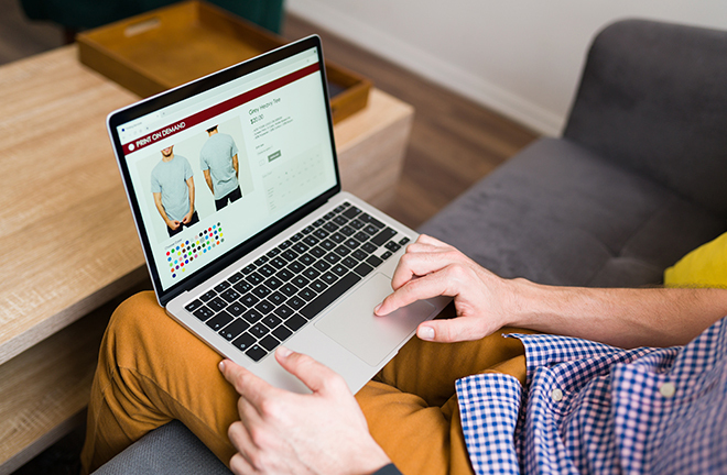 Persona usando una computadora portátil para comprar una camiseta en línea, con imágenes del producto y opciones de color en la pantalla.
