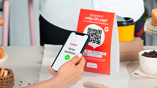 Persona realizando un pago con un teléfono celular mediante un código QR de Getnet exhibido en un mostrador.