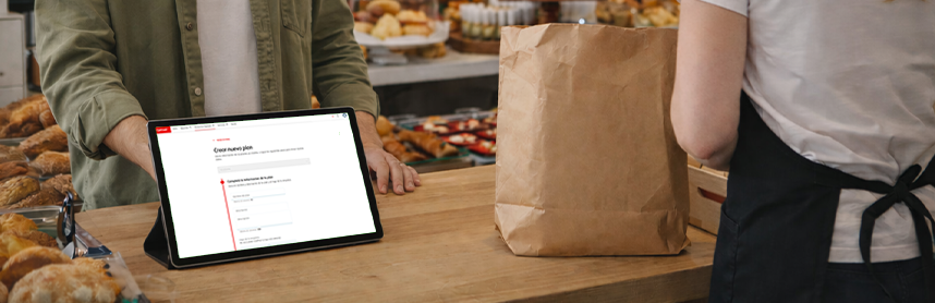 Tablet sobre un mostrador mostrando el Getnet Portal para crear un nuevo plan, junto a una bolsa de papel en un local gastronómico.