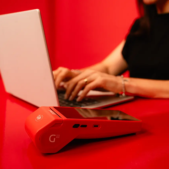 Terminal de cobro Getnet sobre una mesa, mientras una persona trabaja en una notebook al fondo.
