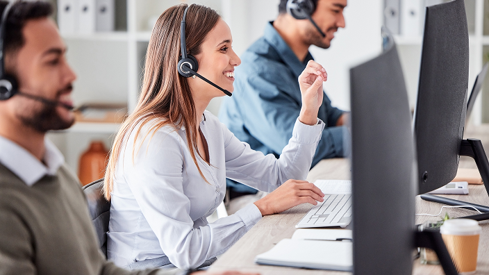 Personas trabajando en un centro de atención al cliente usando auriculares y computadoras.
