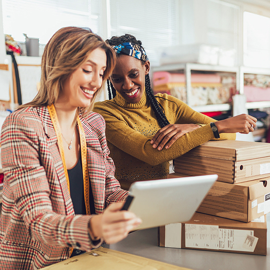 Dos mujeres sonriendo mirando una tablet en un almacén
