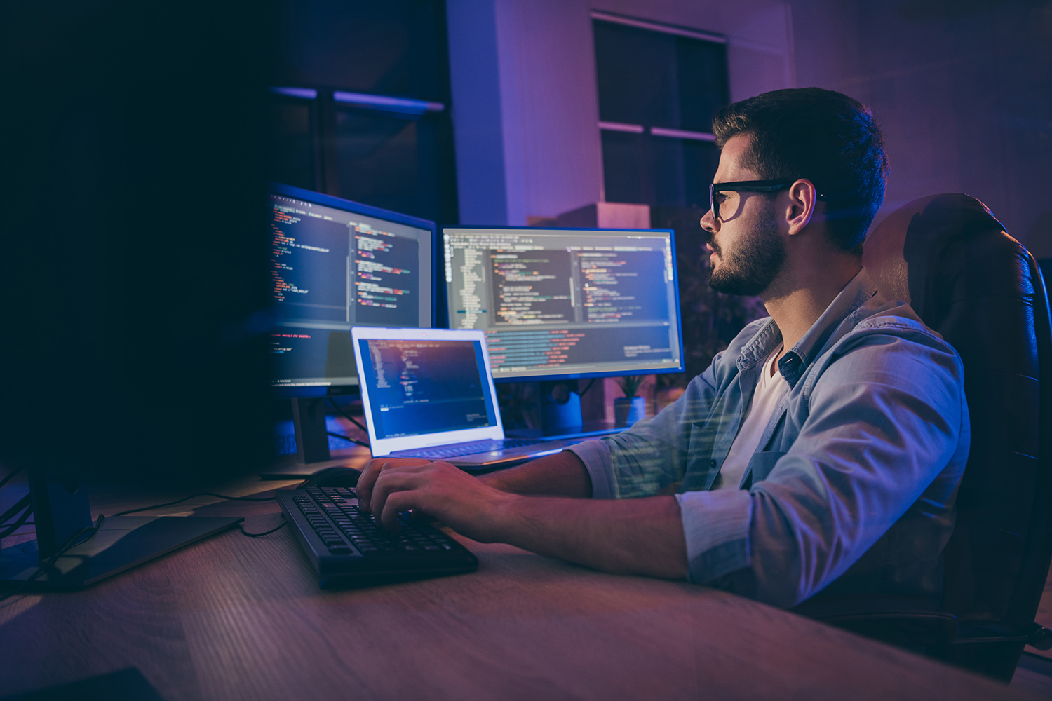 Un programador trabajando en su ordenador con dos pantallas extendidas donde se visualiza un fragmento de código