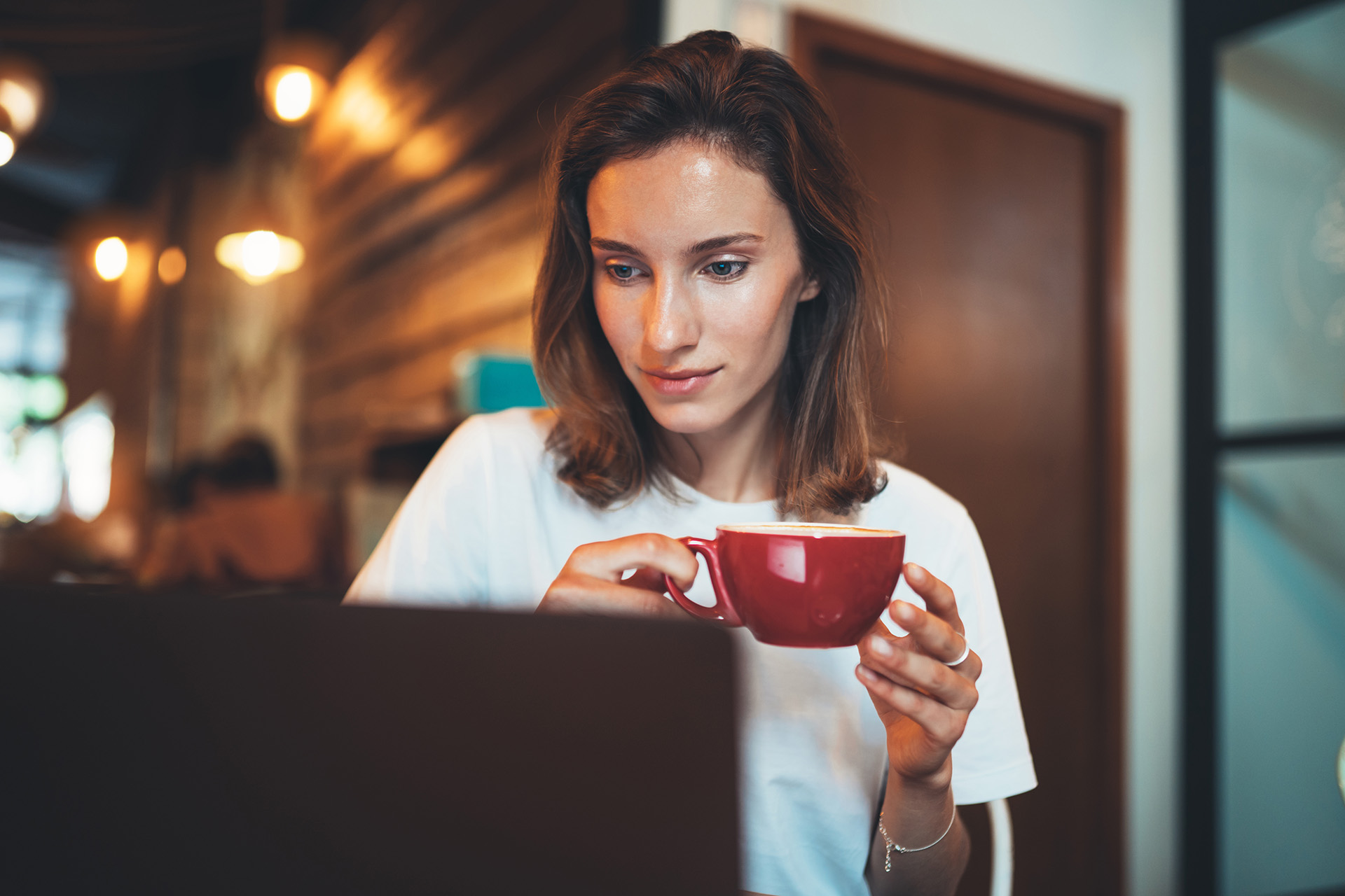 Mujer mirando un ordenador con una taza roja en la mano