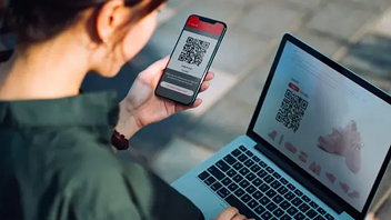 Mujer consultando QR en móvil y ordenador portátil