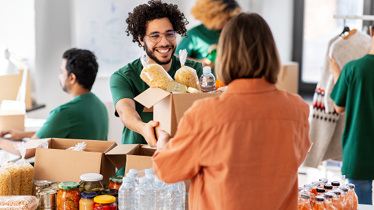 Voluntario con una camiseta verde entregando una caja con alimentos a una mujer