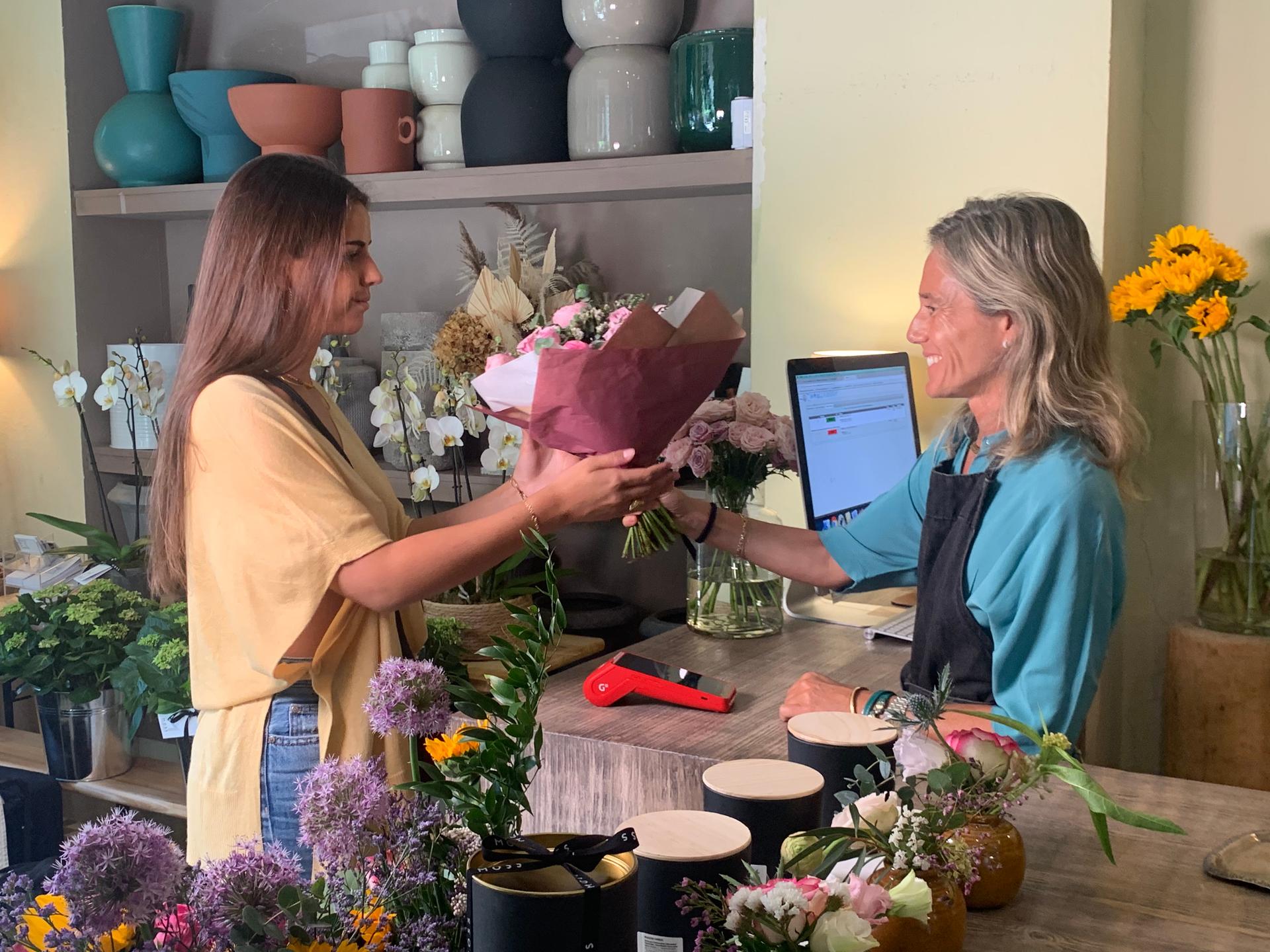 Empleada de floristería entregando un ramo de flores a cliente