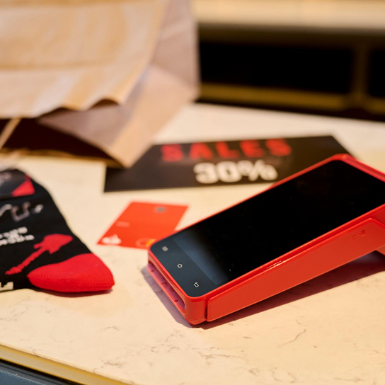Mesa con TPV Getnet, tarjeta del Banco Santander, calcetines rojos y un vale del 30% de descuento