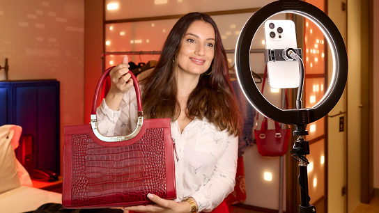 Mujer con un bolso en la mano sonriendo a un celular con un aro selfie
