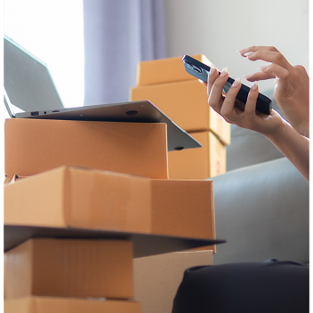 ordenador portáil sobre cajas de cartón y manos usando celular
