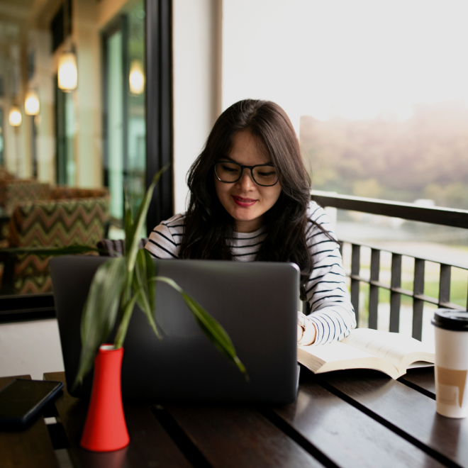Mujer mirando el laptop con un libro a a la derecha
