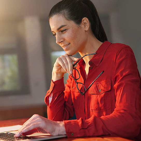 Mulher executiva com camisa vermelha com os oculos na mão contemplando seu portátil