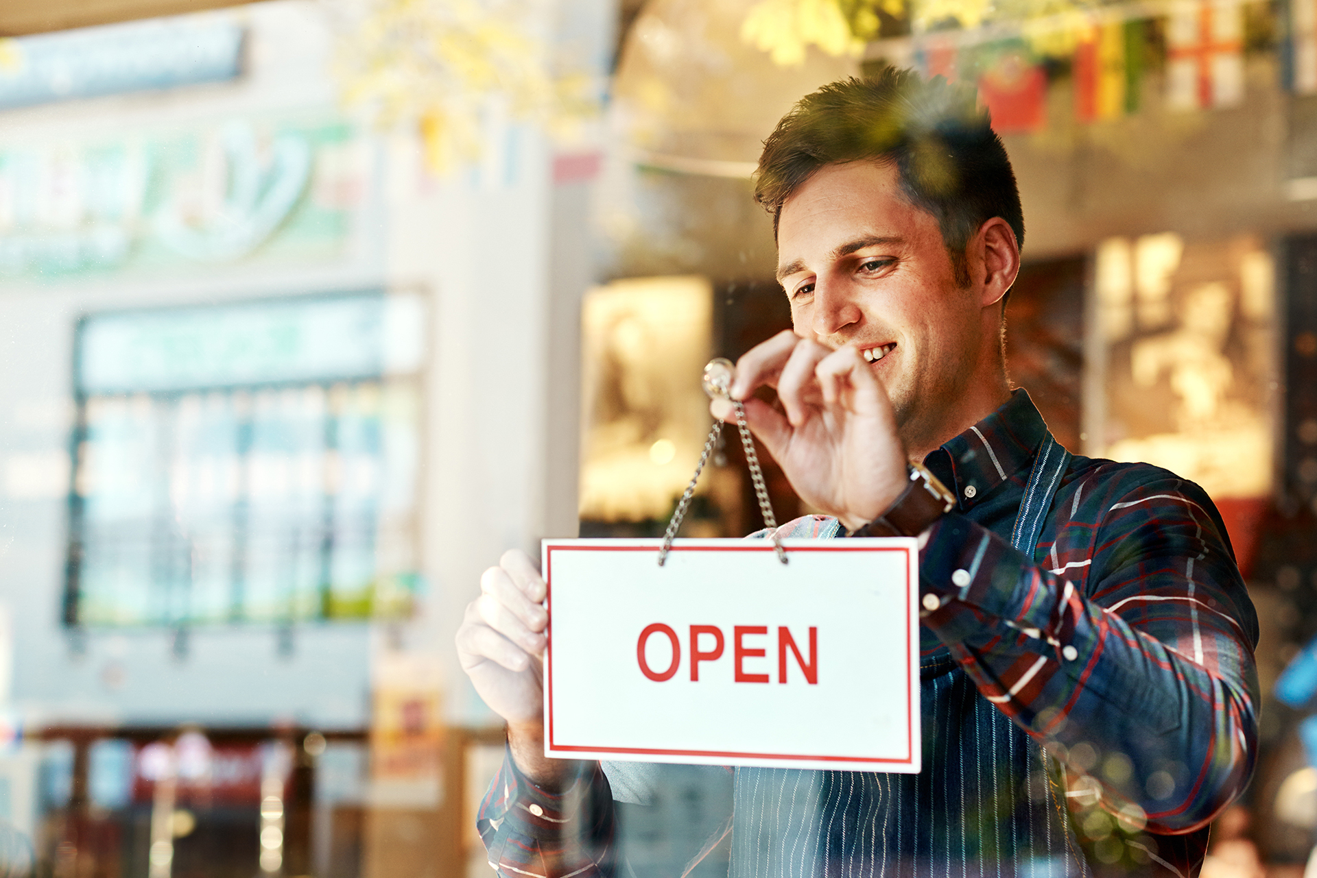 Coffee shop, open sign and a man small business owner standing a glass door for service or hospitality. Cafe, manager or employee with a happy male waiter proud to be opening a new restaurant.