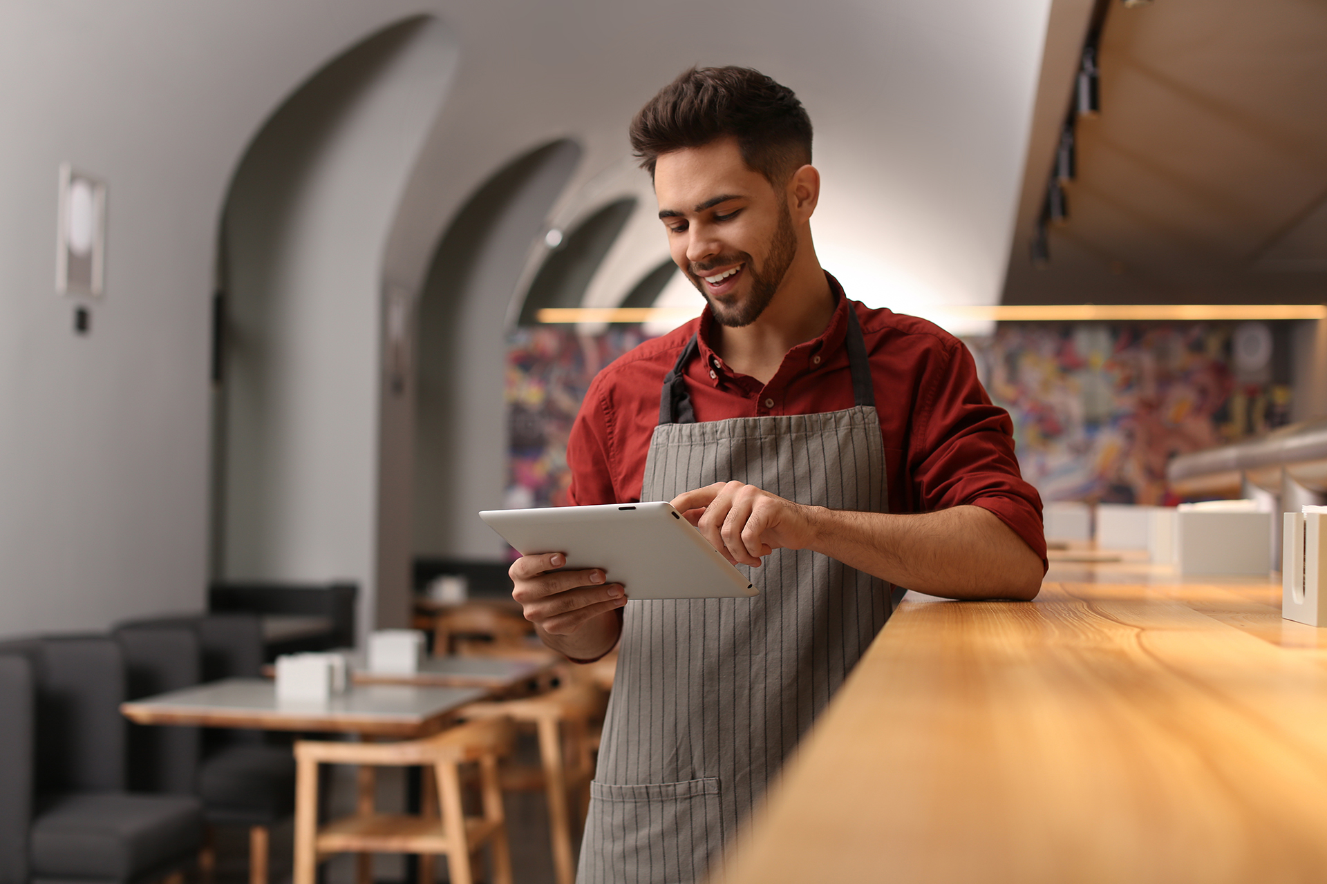 Young male business owner with tablet near counter in his cafe